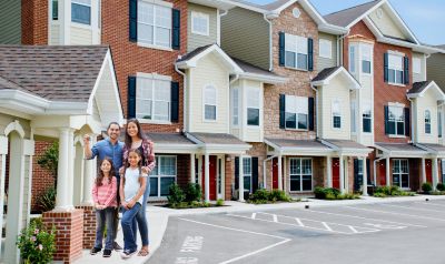 family holding keys in front of a townhouse community showing they just rented the townhouse