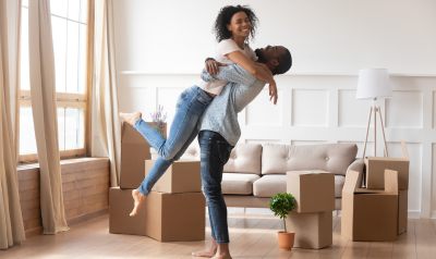a couple with the woman jumping into the arms of the man with moving boxes all around them 